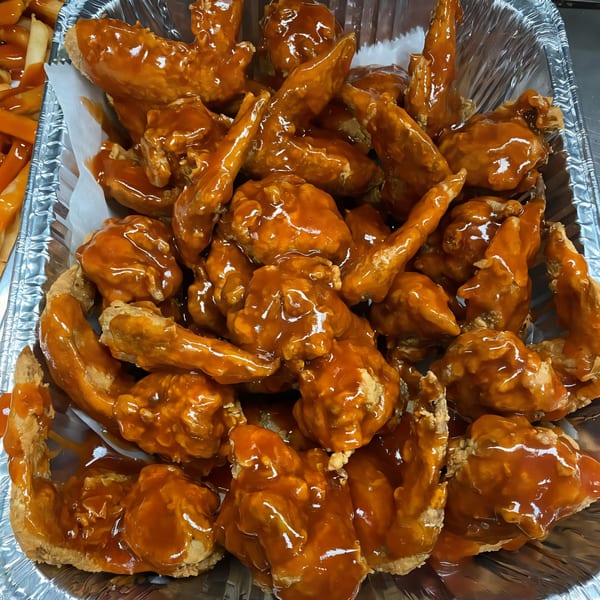A foil pan filled with Harold's Chicken #41 fried chicken wings, generously coated in a glistening orange sauce.