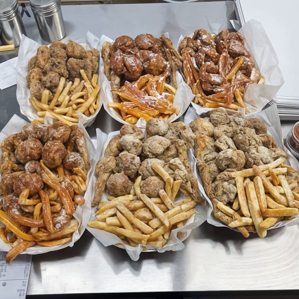 Six baskets of Harold's Chicken and fries, some with powdered sugar, on a metal counter.
